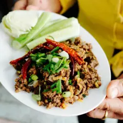 Würziges Laab Moo, ein thailändischer Hackfleischsalat, garniert mit Chili und Frühlingszwiebeln, serviert mit Gurken und Kohl.