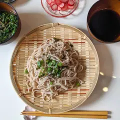 Kalte Soba-Nudeln, garniert mit Frühlingszwiebeln und Nori, serviert auf einem Bambusteller mit Beilagen wie Seetangsalat und Radieschen.