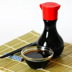 Eine Flasche chinesische Sauce mit Sojasauce, ein Schälchen und Stäbchen auf einer Bambusmatte.