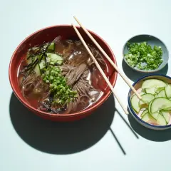 Erfrischendes Mul Naengmyeon mit Buchweizennudeln, Gurkenscheiben, Frühlingszwiebeln und Seetang.