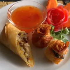 Knusprige Frühlingsrollen und Teigtaschen mit süß-saurer Sauce, garniert mit Karottenblumen. Ein köstlicher Nam Prik Genuss.