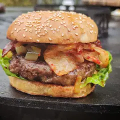 Ein saftiger korean burger mit Kimchi, Gurken und Speck auf einem Sesambrötchen.