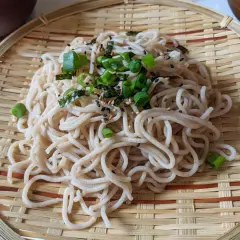 Ein köstlicher soba nudelsalat, garniert mit Frühlingszwiebeln und Sesam, serviert auf einem Bambusteller.