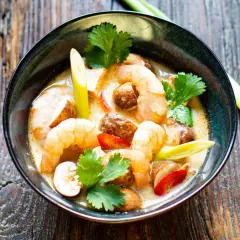 Eine Schüssel mit cremigem Tom Yam Gung, garniert mit Garnelen, Pilzen und Koriander.
