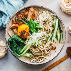 Schüssel mit cremiger Ramen-Suppe, Hühnchen, Ei, Gemüse und frischen **Rahmen Nudeln** daneben.