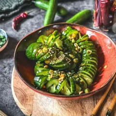 Schmackhafter Gurkensalat asiatisch, garniert mit Sesam und Kräutern, serviert in einer roten Schale mit Stäbchen.