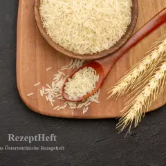 Reis, ein wichtiges Getreide, liegt auf einem Holzlöffel neben einer Schüssel und Ähren.