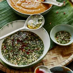 Schalen mit Saucen, darunter eine dunkle, würzige Sauce, die an Hoisin Sauce erinnert, und eine helle Erdnusssauce, auf Bananenblatt auf einem Korbtablett.