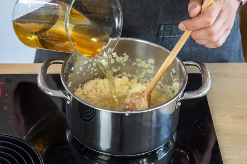 Flüssigkeit wird in einen Topf mit pilaw reis gegossen, während mit einem Holzlöffel gerührt wird.