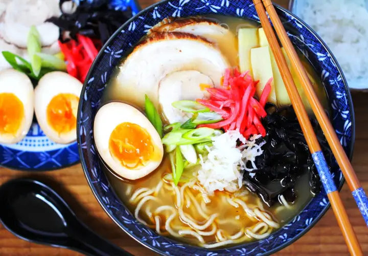 Eine Schüssel Ramen mit perfekt gekochten ramen eiern, Schweinefleisch, Bambussprossen und Frühlingszwiebeln. Daneben liegen weitere halbe Eier.