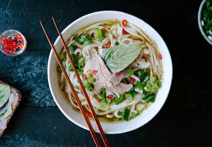 Eine Schüssel dampfendes Pho mit dünnen Rindfleischscheiben, Reisnudeln, Frühlingszwiebeln und Chili. Ein perfektes Pho-Rezept für kalte Tage.