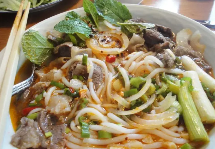 Eine Schüssel Bun Bo Hue mit Rindfleisch, Nudeln, Zwiebeln, Frühlingszwiebeln und Minze.