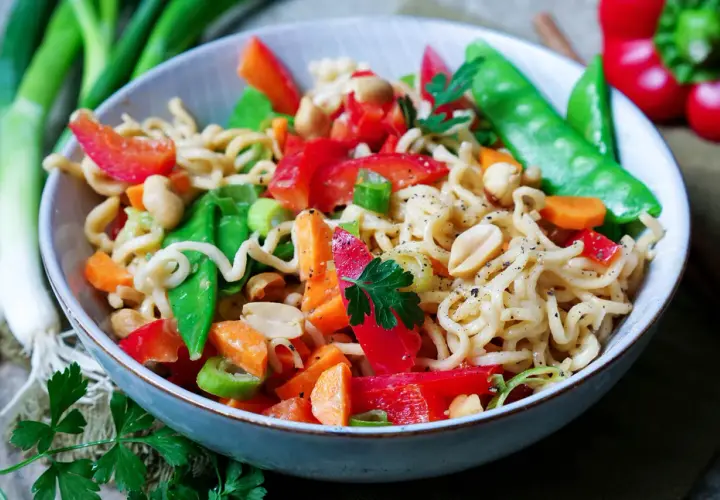 Bunter mie nudelsalat mit Erdnüssen, Paprika, Zuckerschoten und Karotten, garniert mit Petersilie.