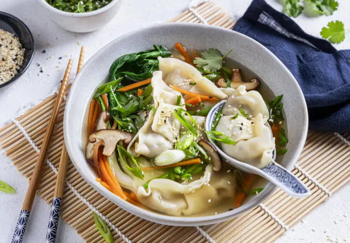 Eine dampfende Schüssel **Wantan Suppe** mit zarten Teigtaschen, Shiitake-Pilzen, Karotten und Frühlingszwiebeln, garniert mit Sesam.