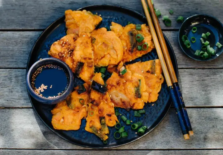 Knusprige Kimchi-Pfannkuchen mit Frühlingszwiebeln und Sesam, serviert mit Dip und Stäbchen.