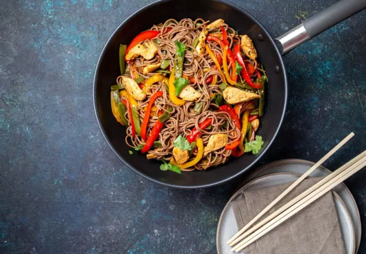 Wok-Gericht mit chinesischen Eiernudeln, Hähnchenstreifen und bunten Paprikastreifen, garniert mit Koriander.