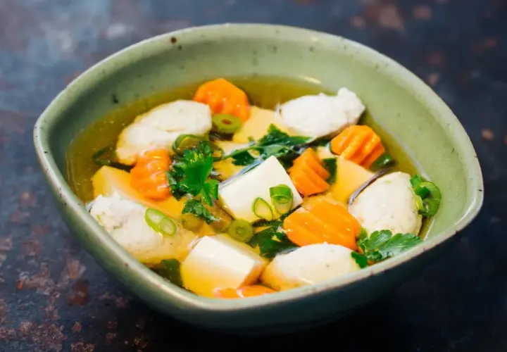 Eine Schüssel Hu Tieu Suppe mit Tofu, Karotten und Fleischbällchen, garniert mit Frühlingszwiebeln und Petersilie.