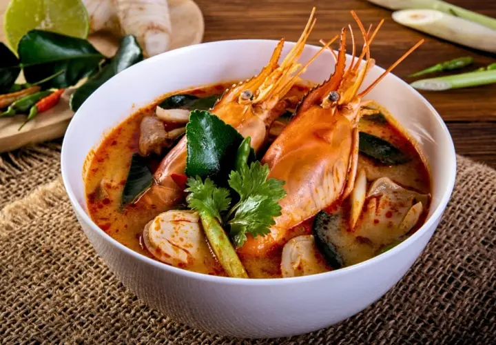 Eine Schüssel Tom Yum Suppe mit Garnelen, Pilzen und Kaffirlimettenblättern, garniert mit Koriander.