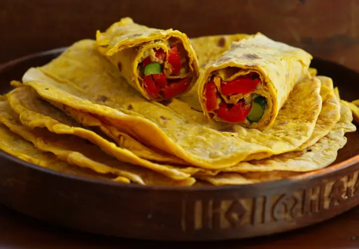 Chapati-Rezept: Fladenbrot gefüllt mit roten Paprika und Gurke, auf einem Stapel weiterer Chapati in einer Holzschale.