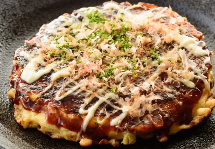 Ein herzhaftes Okonomiyaki Hiroshima, übergossen mit Sauce und Mayonnaise, bestreut mit Bonitoflocken und Schnittlauch.