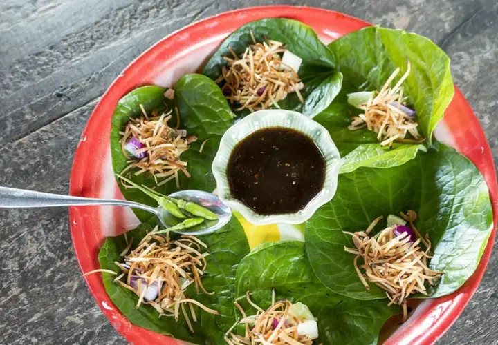 Miang Kham: grüne Blätter gefüllt mit knusprigen Nüssen, Zwiebeln und Limette, serviert mit Dip und Chilis.
