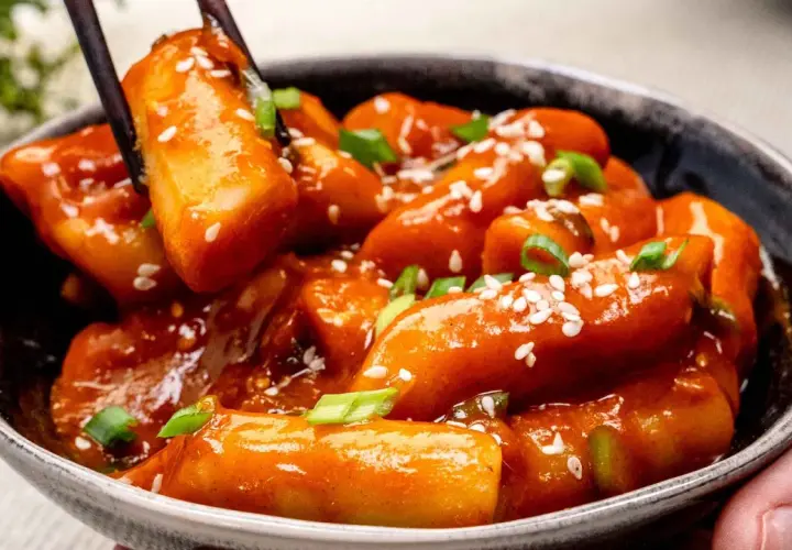 Schüssel mit würzigem Tteokbokki, Reiskuchen in scharfer Sauce, garniert mit Sesam und Frühlingszwiebeln.