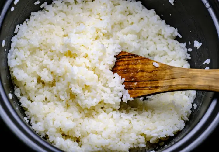 Frisch gekochter Reis wird mit einem Holzlöffel vermischt, bereit für Sushi-Essig.