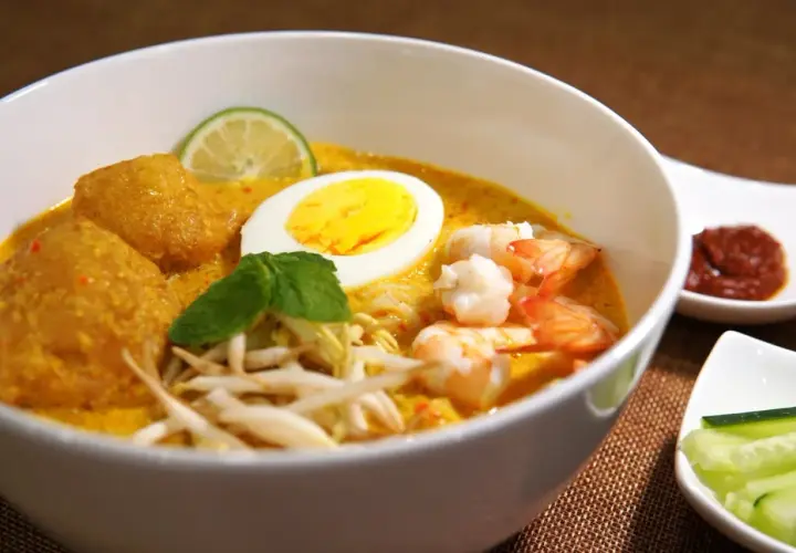 Schüssel mit cremigem Laksa-Rezept, Garnelen, Ei, frischen Sprossen und Limette.