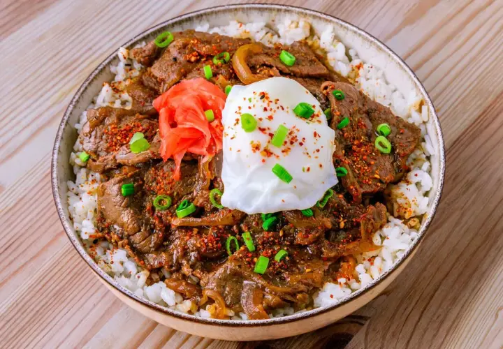 Eine köstliche japanische Bowl mit Reis, zartem Rindfleisch, einem pochierten Ei, eingelegtem Ingwer und Frühlingszwiebeln.
