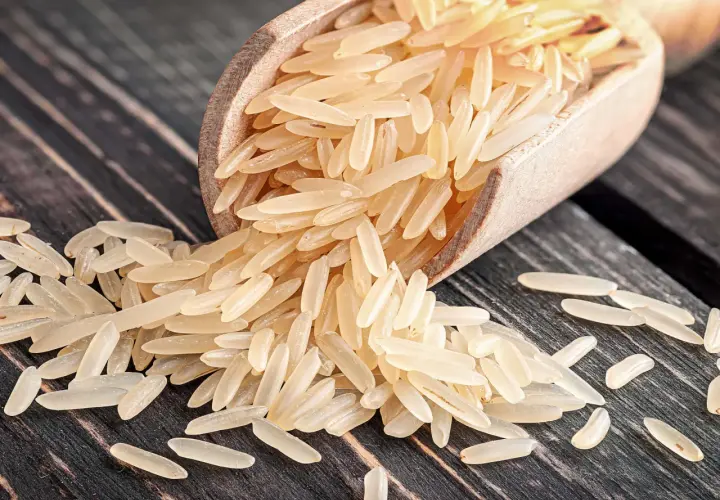 Ein Holzlöffel voller heller Reiskörner, die auf einer dunklen Holzoberfläche verstreut sind. Dies ist ein Beispiel für Rundkornreis.