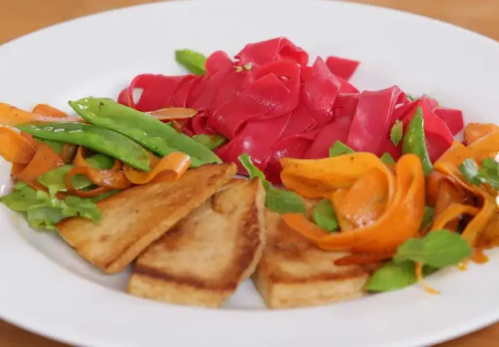 Bunte Reisnudeln kochen mit gebratenem Tofu, Karotten und Zuckerschoten. Ein farbenfrohes Gericht, das Lust auf mehr macht.