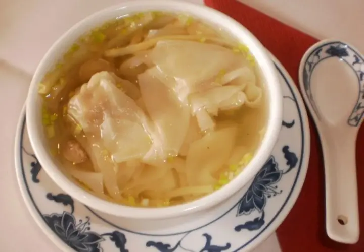 Eine Schüssel mit dampfender Wan-Tan-Suppe, gefüllt mit zarten Teigtaschen und Garnelen, bereit zum Genießen.