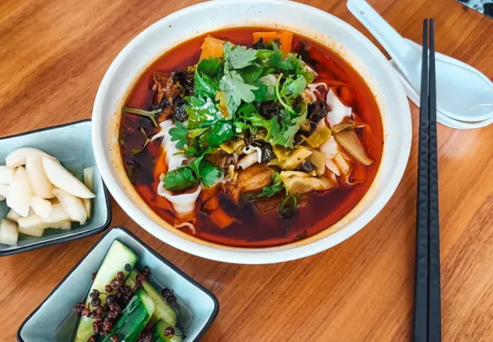 Eine Schüssel Niu Rou Mian, garniert mit Koriander, daneben eingelegte Gurken und Rettich.