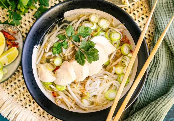 Eine dampfende Schüssel vietnamesische Reissuppe mit zarten Hühnerbrustscheiben, Reisnudeln, Sojasprossen und Frühlingszwiebeln.