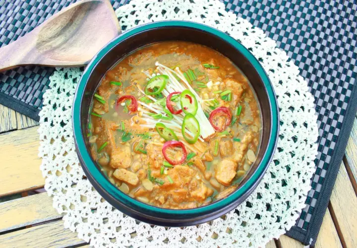 Herzhafte Doenjang Suppe mit Enoki-Pilzen und scharfen Chilischeiben, serviert in einer traditionellen Schüssel.
