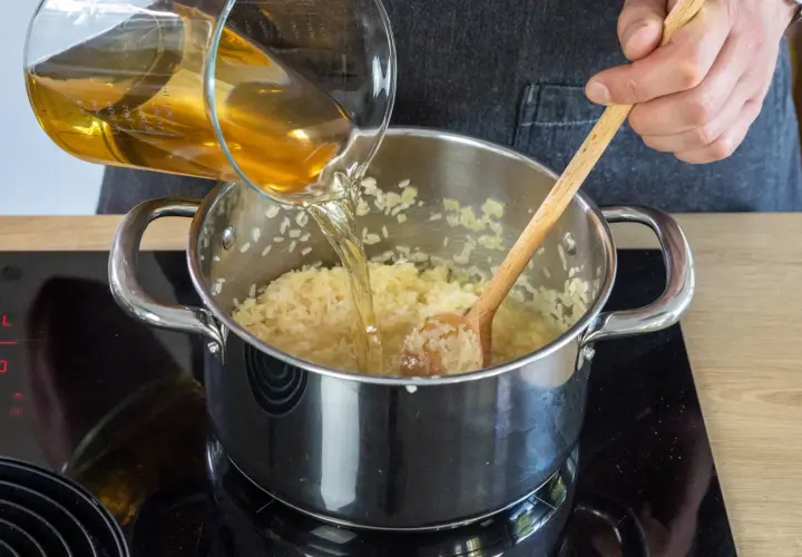 Flüssigkeit wird in einen Topf mit pilaw reis gegossen, während mit einem Holzlöffel gerührt wird.