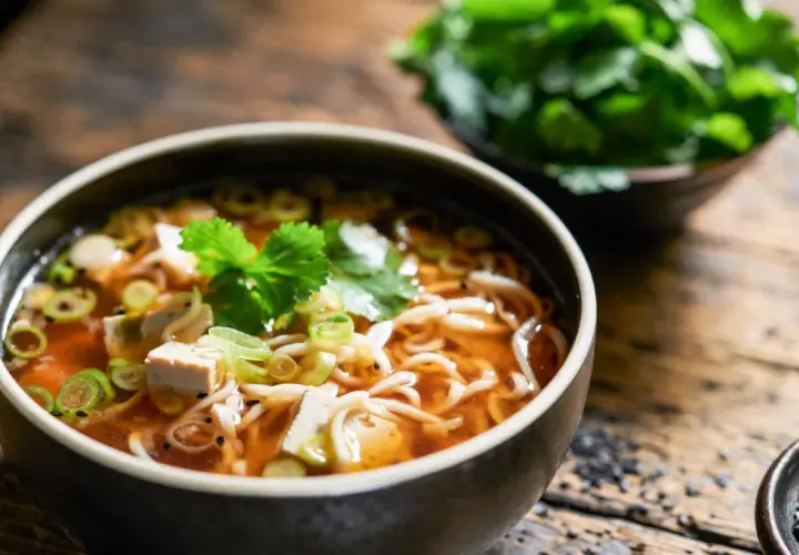 Eine dampfende Schüssel Miso Suppe mit Tofu, Nudeln und Frühlingszwiebeln, garniert mit frischer Petersilie.