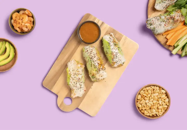 Frische Sommerrollen mit Hoisin-Sauce, Garnelen, Avocado und Erdnüssen auf lila Hintergrund.