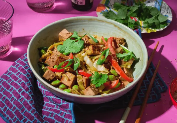 Schüssel mit spitzkohl asiatisch vegetarisch, Tofu, Edamame und Koriander. Dazu Stäbchen und ein Glas Wasser.
