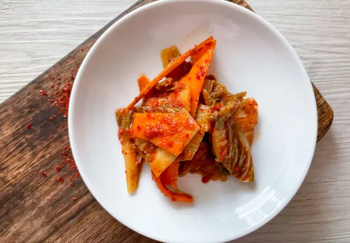 Frisch zubereitetes Kimchi, ein köstliches Rezept, serviert auf einem weißen Teller mit karamellisierten Karottenstreifen und Chinakohl.