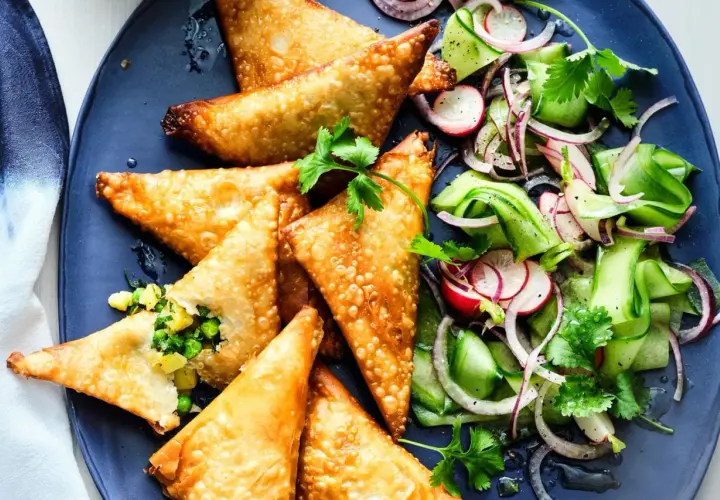 Goldbraune, knusprige Samosas mit Erbsen- und Kartoffelfüllung, serviert mit einem frischen Gurken-Radieschen-Salat. Ein leckeres samosas rezept.