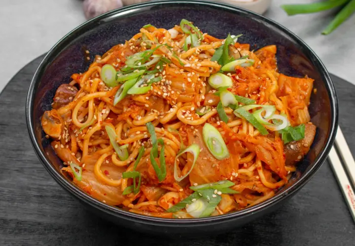 Eine Schüssel mit würzigem Kimchi Ramen, garniert mit Frühlingszwiebeln und Sesam.
