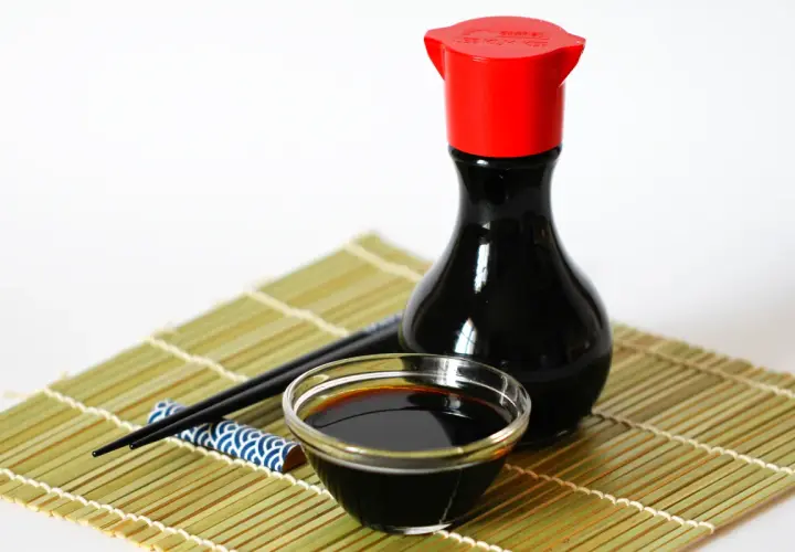Eine Flasche chinesische Sauce mit Sojasauce, ein Schälchen und Stäbchen auf einer Bambusmatte.