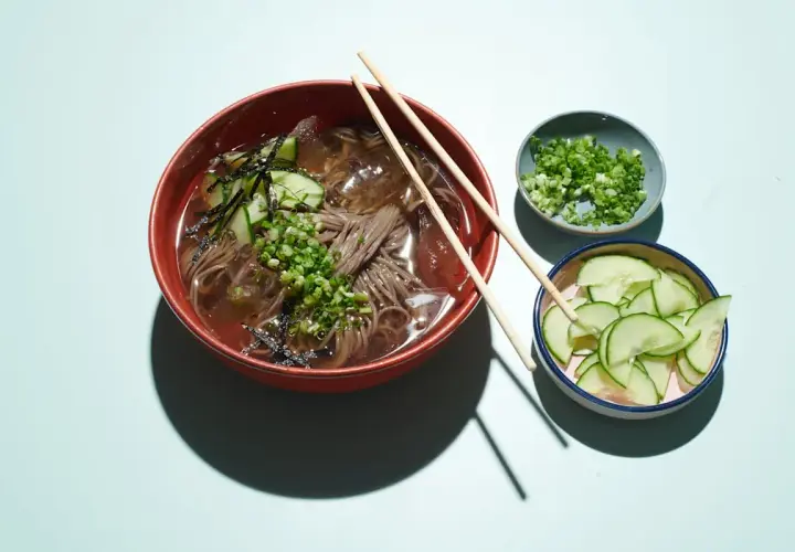 Erfrischendes Mul Naengmyeon mit Buchweizennudeln, Gurkenscheiben, Frühlingszwiebeln und Seetang.