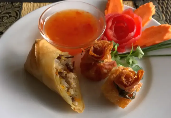 Knusprige Frühlingsrollen und Teigtaschen mit süß-saurer Sauce, garniert mit Karottenblumen. Ein köstlicher Nam Prik Genuss.