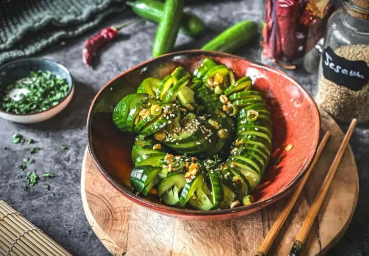 Schmackhafter Gurkensalat asiatisch, garniert mit Sesam und Kräutern, serviert in einer roten Schale mit Stäbchen.