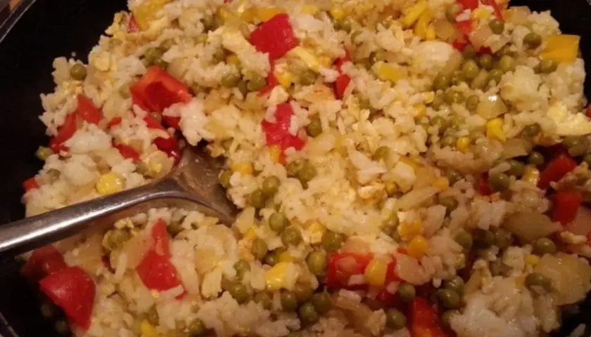 Ein köstlicher kantonesischer Reis mit Erbsen, Paprika und Mais, serviert in einer Pfanne.