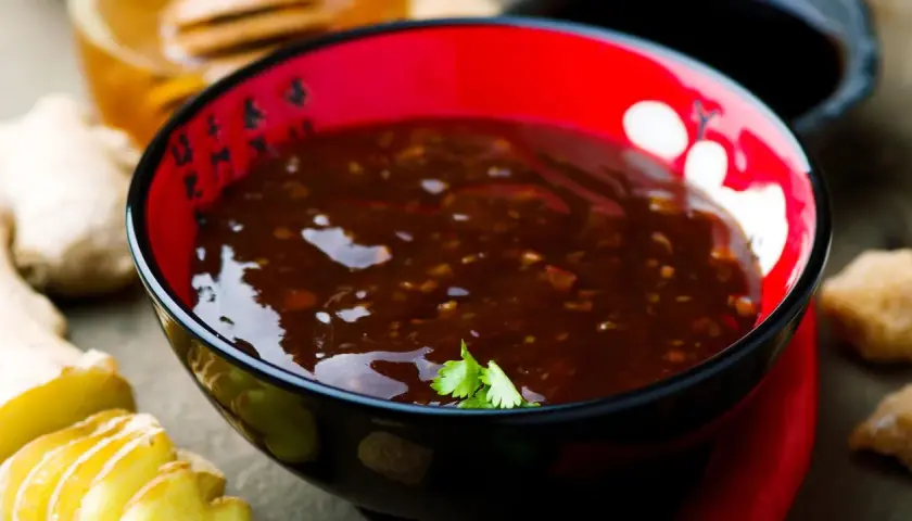 Schwarze Schale mit Teriyaki-Sauce, Ingwer und Honig. Der Geschmack von Teriyaki-Sauce ist süßlich-salzig und würzig.