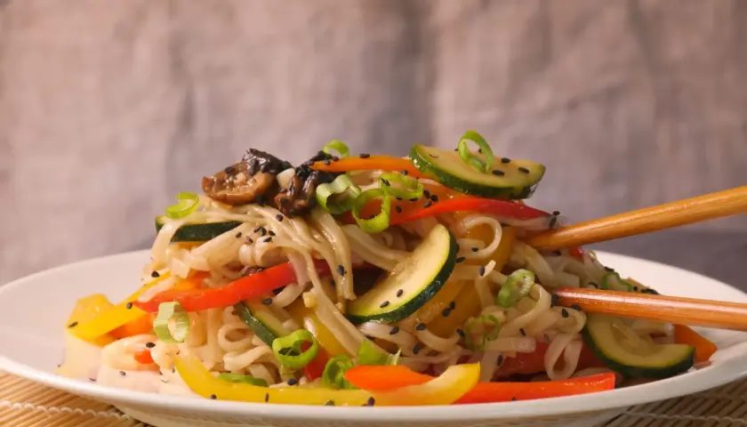Reisnudeln mit bunten Paprikastreifen, Zucchini und Pilzen, garniert mit Frühlingszwiebeln und Sesam. Ein leckeres Gericht, das zum Genießen einlädt.
