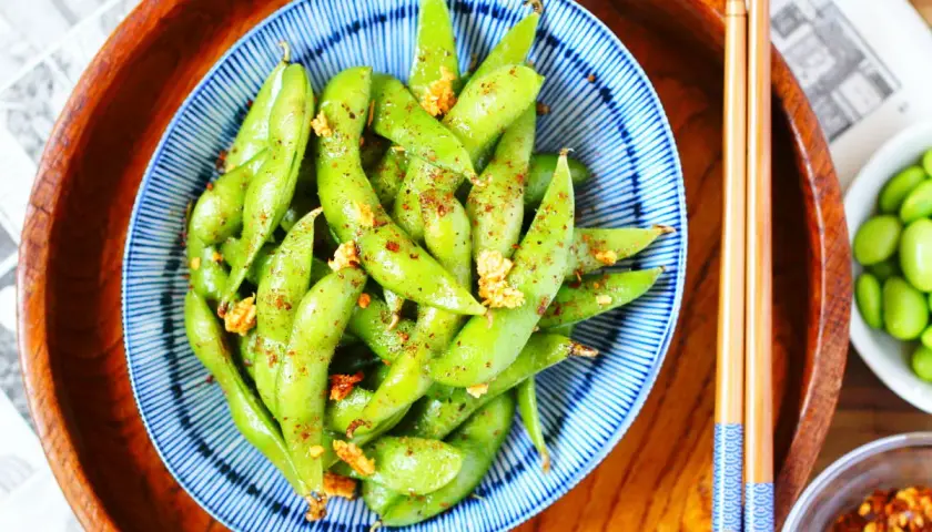 Schüssel mit gewürzten Edamame-Schoten, eine gesunde Quelle für Edamame Proteine, bereit zum Genuss mit Stäbchen.